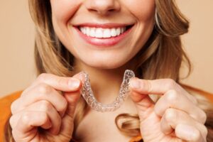 woman smiling holding up her invisalign clear aligner