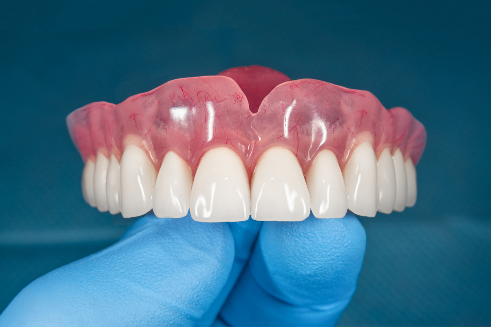 Denture.,Full,Removable,Denture,Of,The,Upper,Jaw,Of,Man Dentures being held by a gloved hand, showcasing a realistic dental prosthesis with pink gum base and white teeth, relevant to restorative dental services for patients seeking complete tooth replacement.