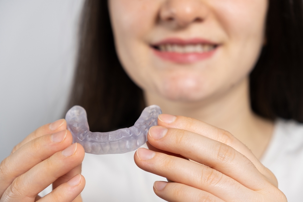 Woman holding a custom nightguard for dental protection, smiling, emphasizing solutions for teeth clenching and grinding during the holidays.