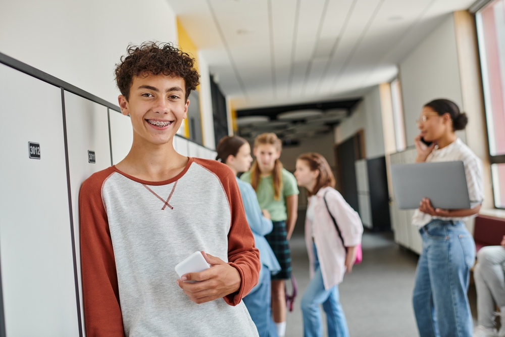 Happy,Boy,With,Braces,Holding,Smartphone,And,Looking,At,Camera teen boy with braces at school
